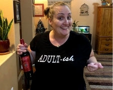 Woman wearing a shirt that says "adultish" and holding a bottle of wine